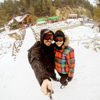 Attractive couple taking awesome selfie with a wooden cabin cove Attractive couple taking awesome selfie with a wooden cabin covered in snow in the background.